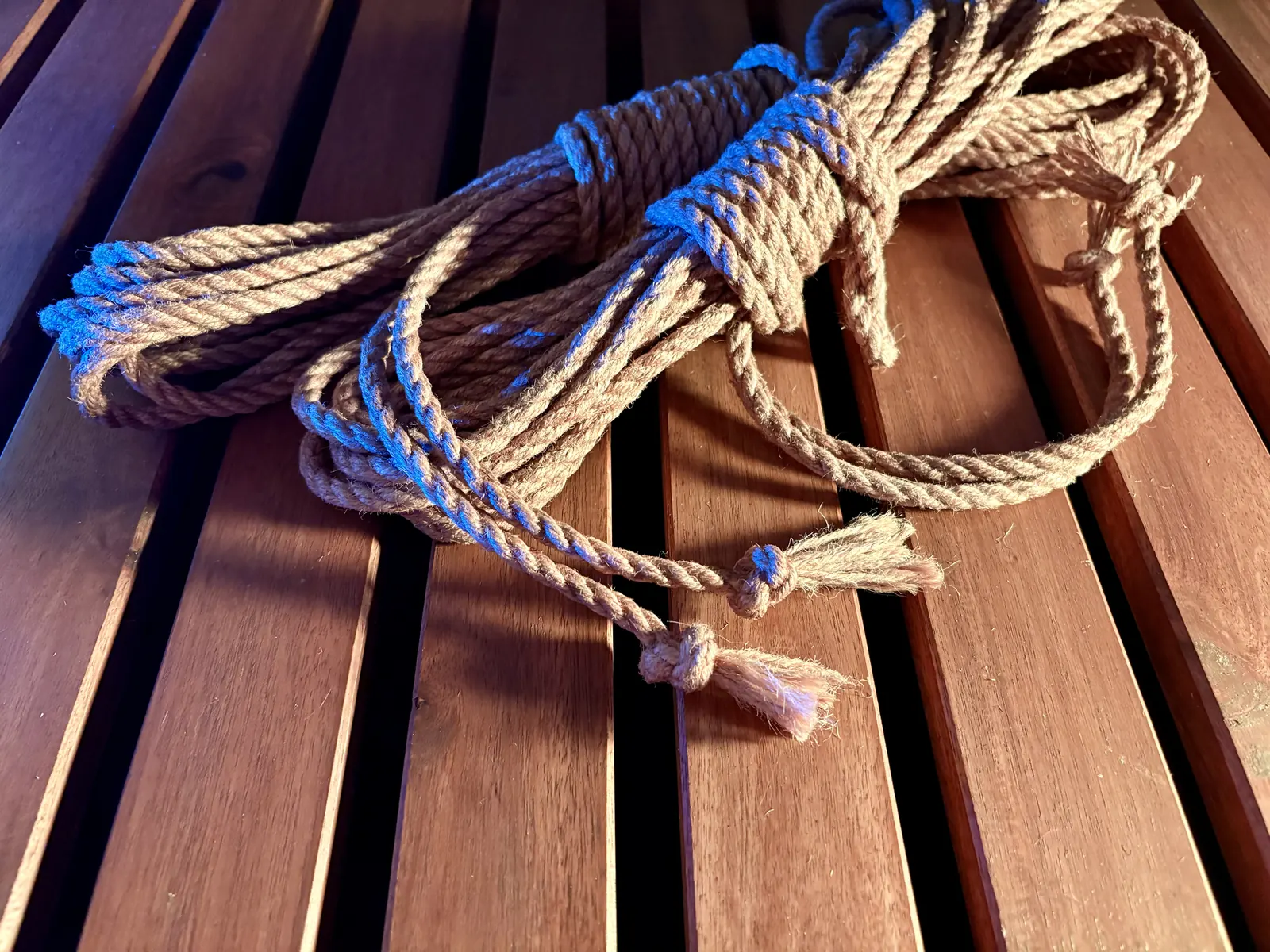 Two coiled lengths of natural fibre rope with knotted ends, resting on a wooden slatted table.
